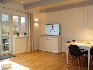 A modern dining area with a television mounted on the wall, a white cabinet below, and a wooden dining table with chairs. - 4 Caymans at Boldix House (Wyk auf Foehr)