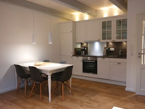 A modern kitchen with white cabinetry, a central island, and a dining area with a white table and black chairs. - 4 Caymans at Boldix House (Wyk auf Foehr)