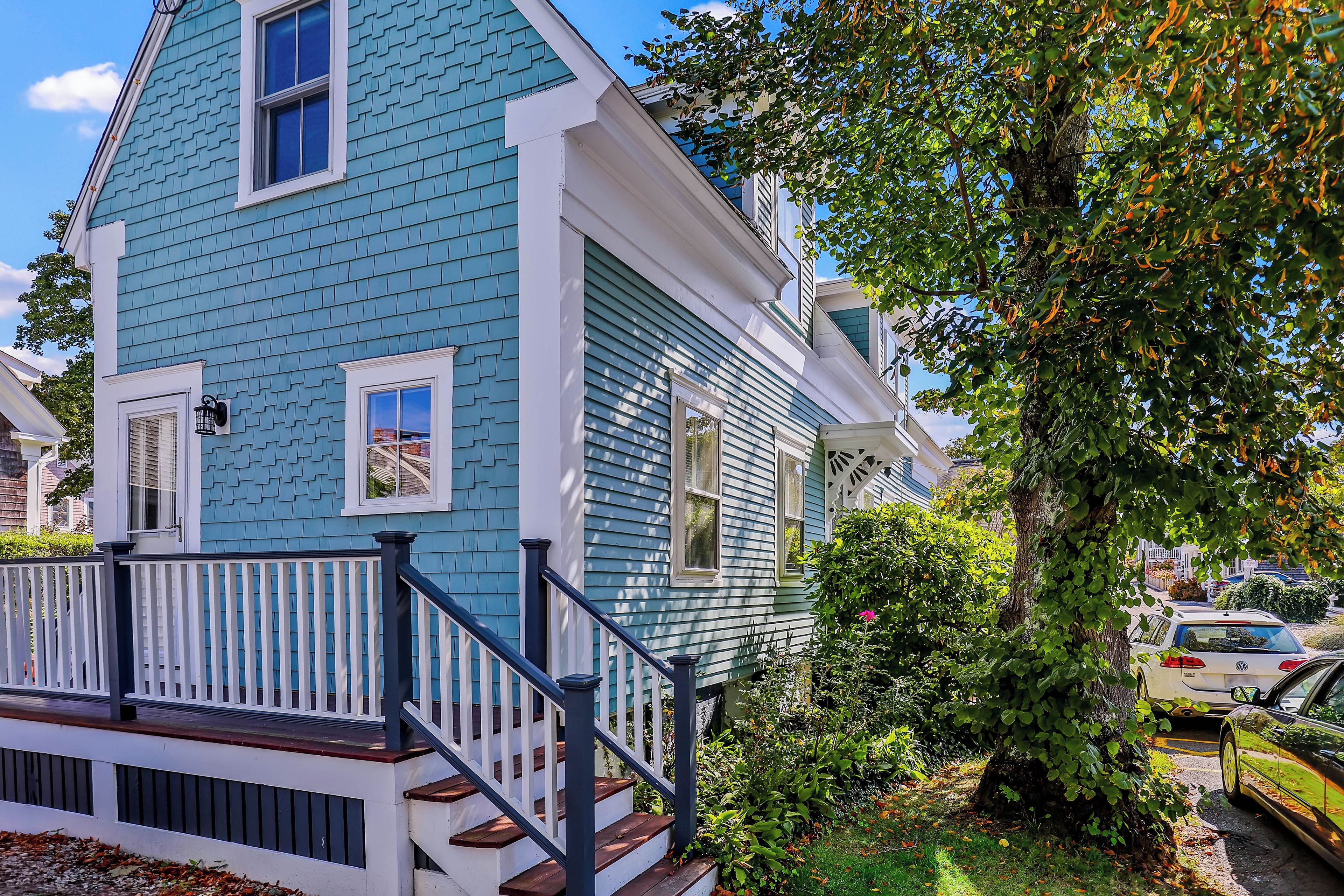A two-story house with a blue exterior, white trim, and a front porch with a black railing.