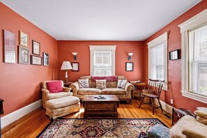 A living room with a sofa, armchair, coffee table, and a patterned rug. - Historic Ptown Charm - 3BR, Yard, AC, Parking (Provincetown)