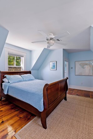 Un dormitorio con una cama de madera, un ventilador de techo, una ventana y un mapa en la pared.