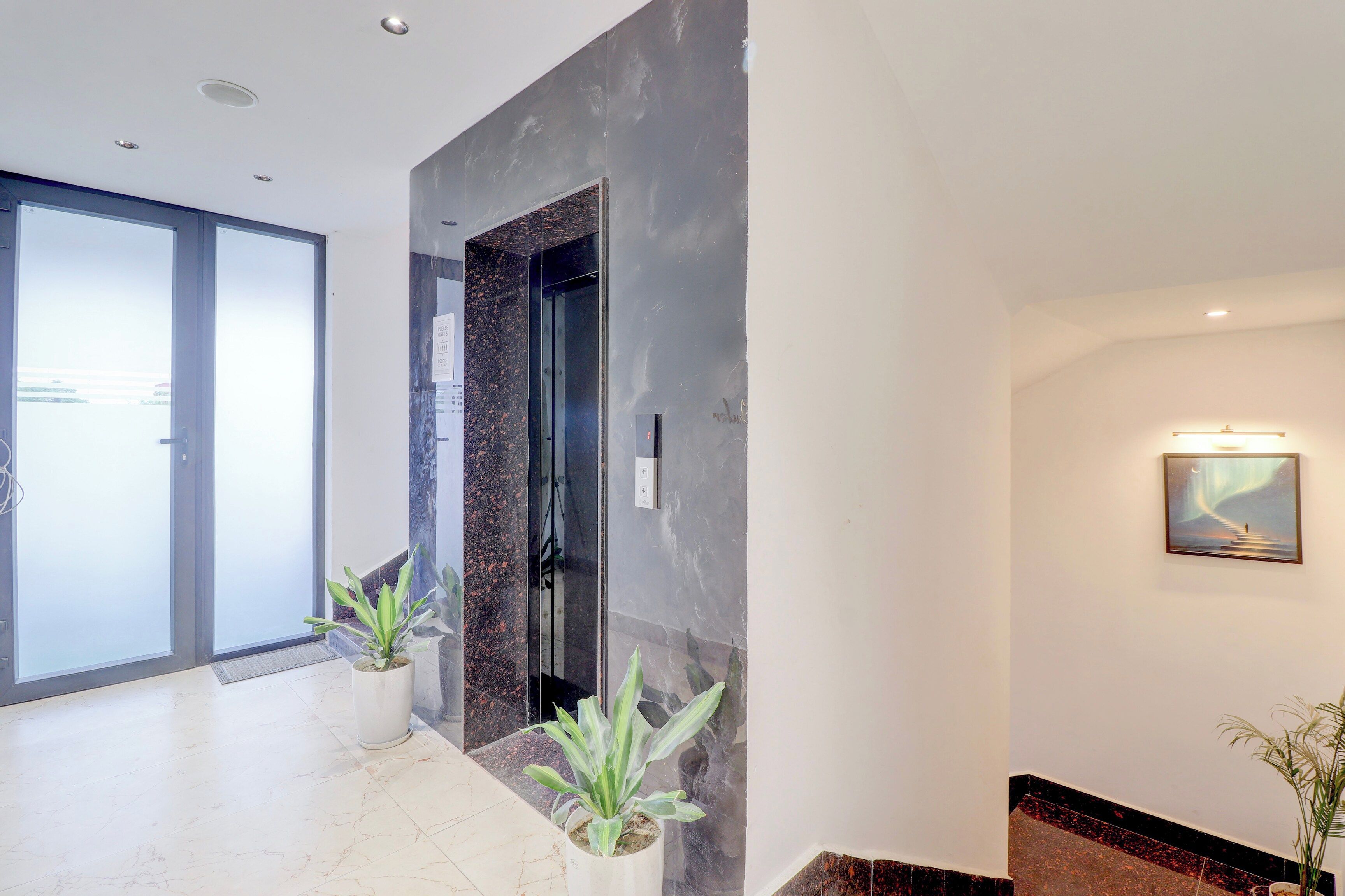 Una hall moderna con ingresso tramite porta in vetro, parete in marmo e un quadro appeso.