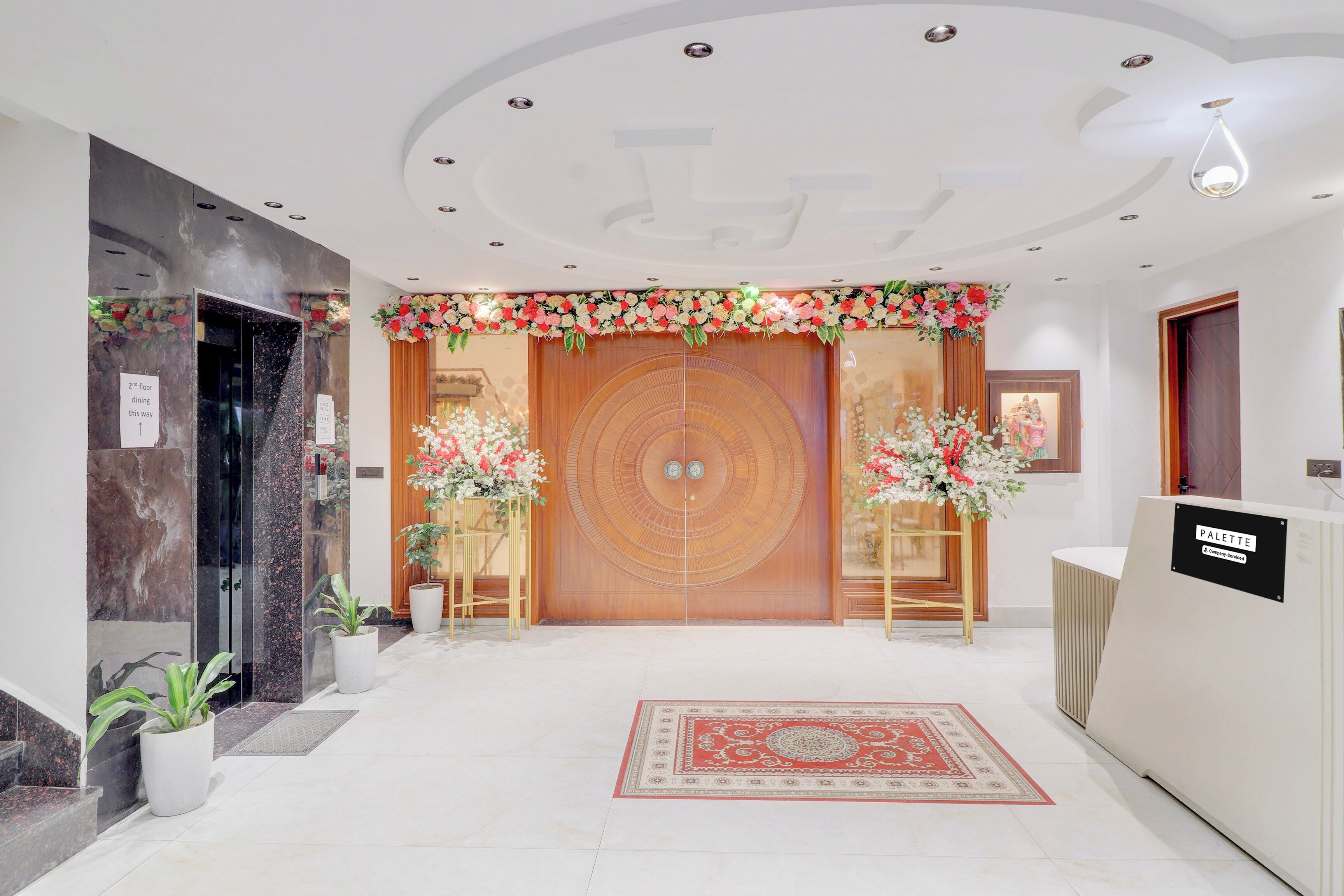 Un vestíbulo de hotel con mostrador de recepción, una puerta de madera con diseño circular y un arreglo floral sobre la puerta.