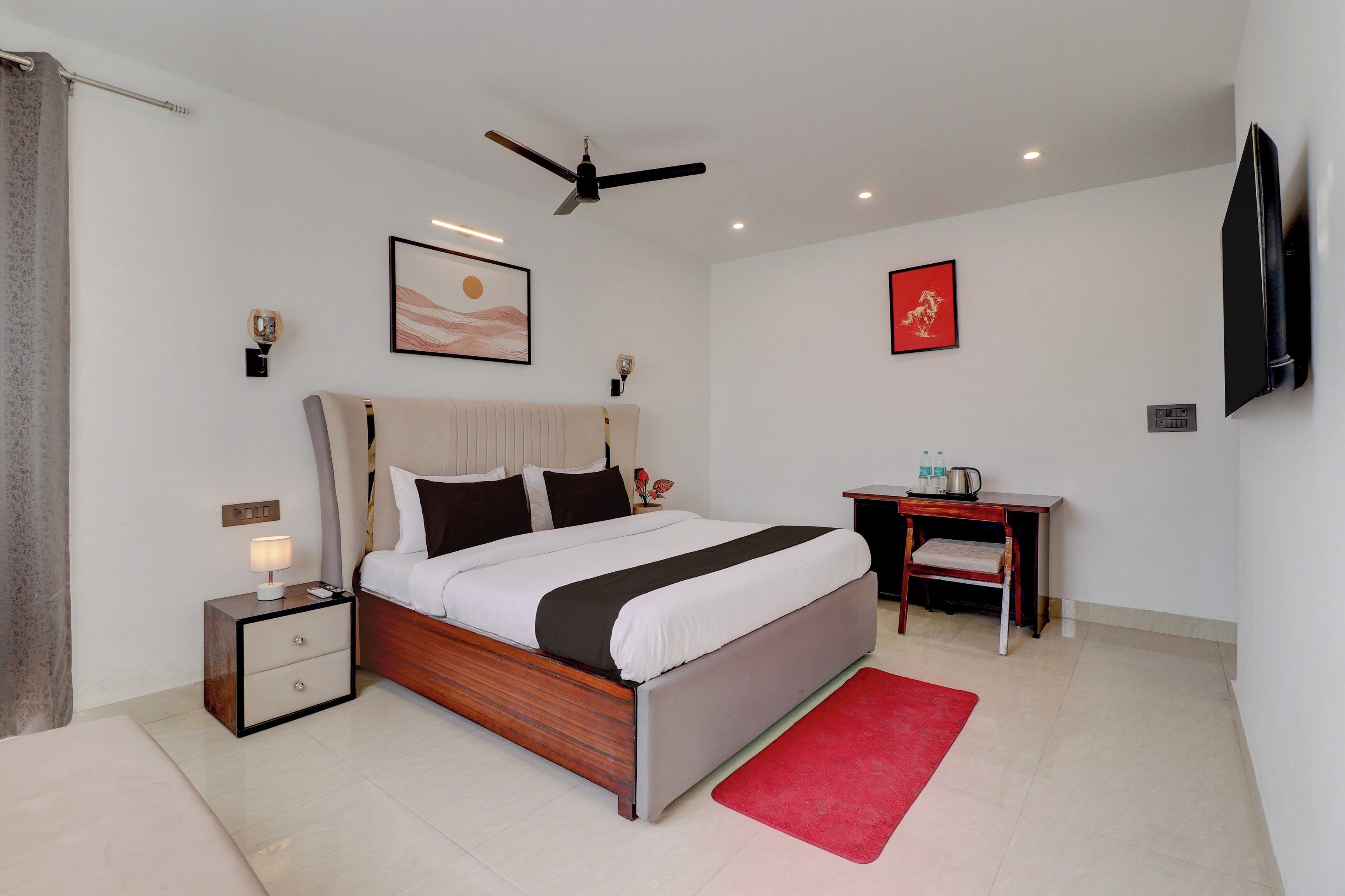 Habitación de hotel con cama, mesita de noche, lámpara, obra de arte, ventilador de techo y escritorio con silla.