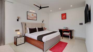 Habitación de hotel con cama, mesita de noche, lámpara, obra de arte, ventilador de techo y escritorio con silla.
