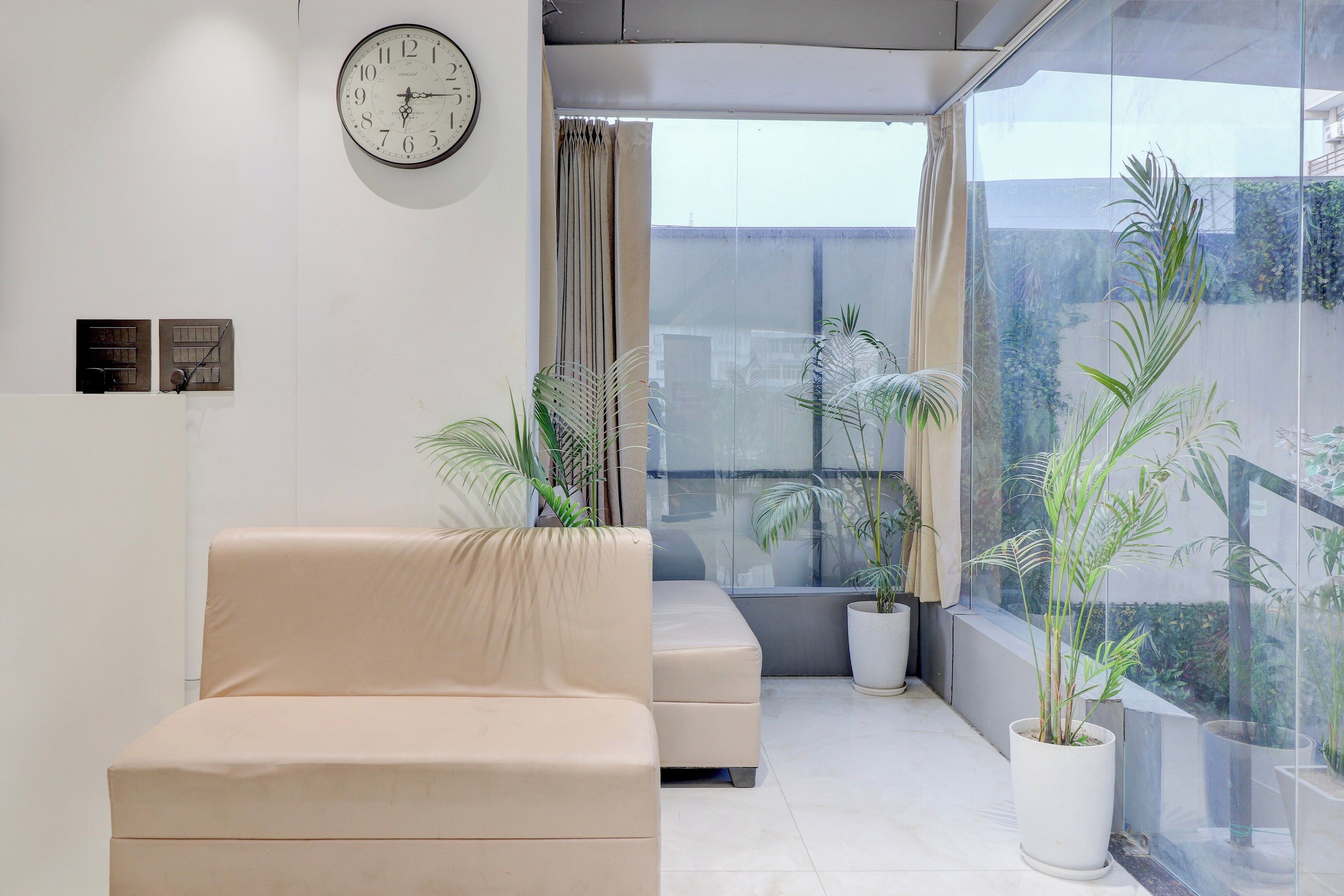 Ein modernes Wohnzimmer mit einem beigefarbenen Sofa, einer Wanduhr und Zimmerpflanzen.