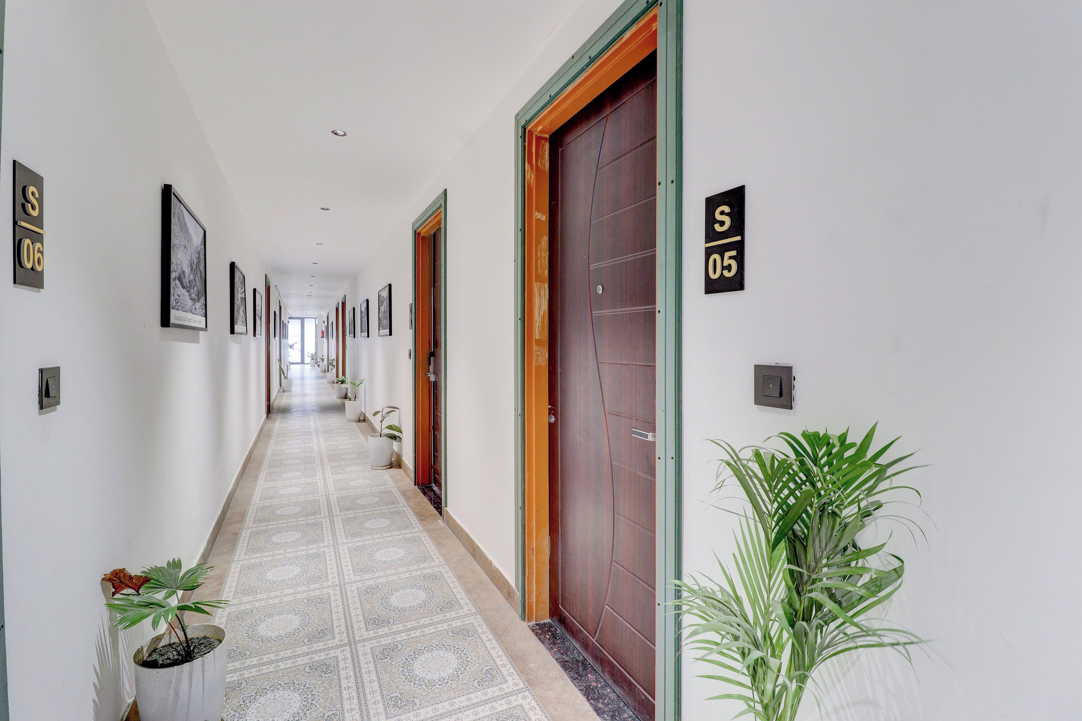 A hallway with numbered doors, potted plants, and framed pictures on the walls.