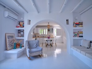 A spacious living area with a dining table and chairs, a sofa, and bookshelves. - Villa Kyma - Greek Summer (Kamares Naousas)