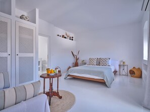 A bedroom with a bed, a sofa, a small table with fruit, and a decorative wall piece. - Villa Kyma - Greek Summer (Kamares Naousas)