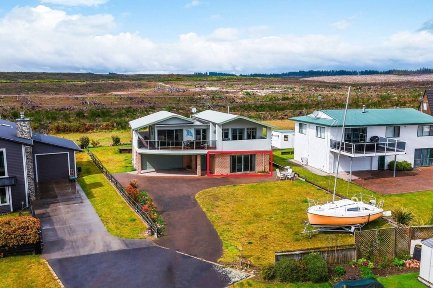 Et moderne hus med to etager, stor garage, båd i havnen og udsigt til et naturområde i baggrunden.