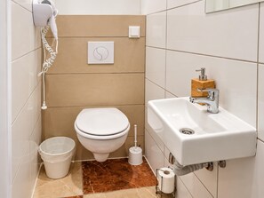 A bathroom with a toilet, sink, hairdryer, and a toilet paper holder. - A Month in Vienna 1BR Apartment (Wien)