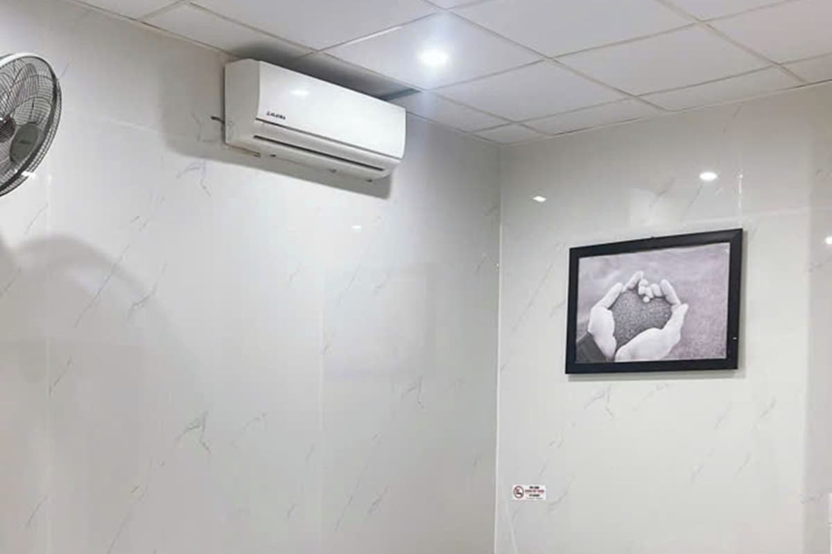 A hotel room with a bed, two wooden chairs, a small table, an air conditioning unit, and a framed picture on the wall.