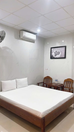 A hotel room with a bed, two wooden chairs, a small table, an air conditioning unit, and a framed picture on the wall. - BLUE LANTERN HOMESTAY (HOI AN)