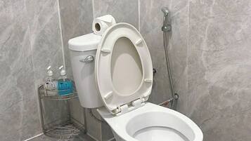 Une salle de bain équipée de toilettes, d’un sèche-mains et d’une pomme de douche.
