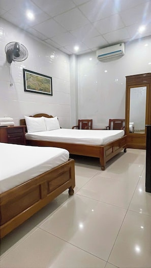 A hotel room with two wooden beds, a bedside table, a chair, a standing fan, an air conditioning unit, and a framed picture on the wall. - BLUE LANTERN HOMESTAY (HOI AN)