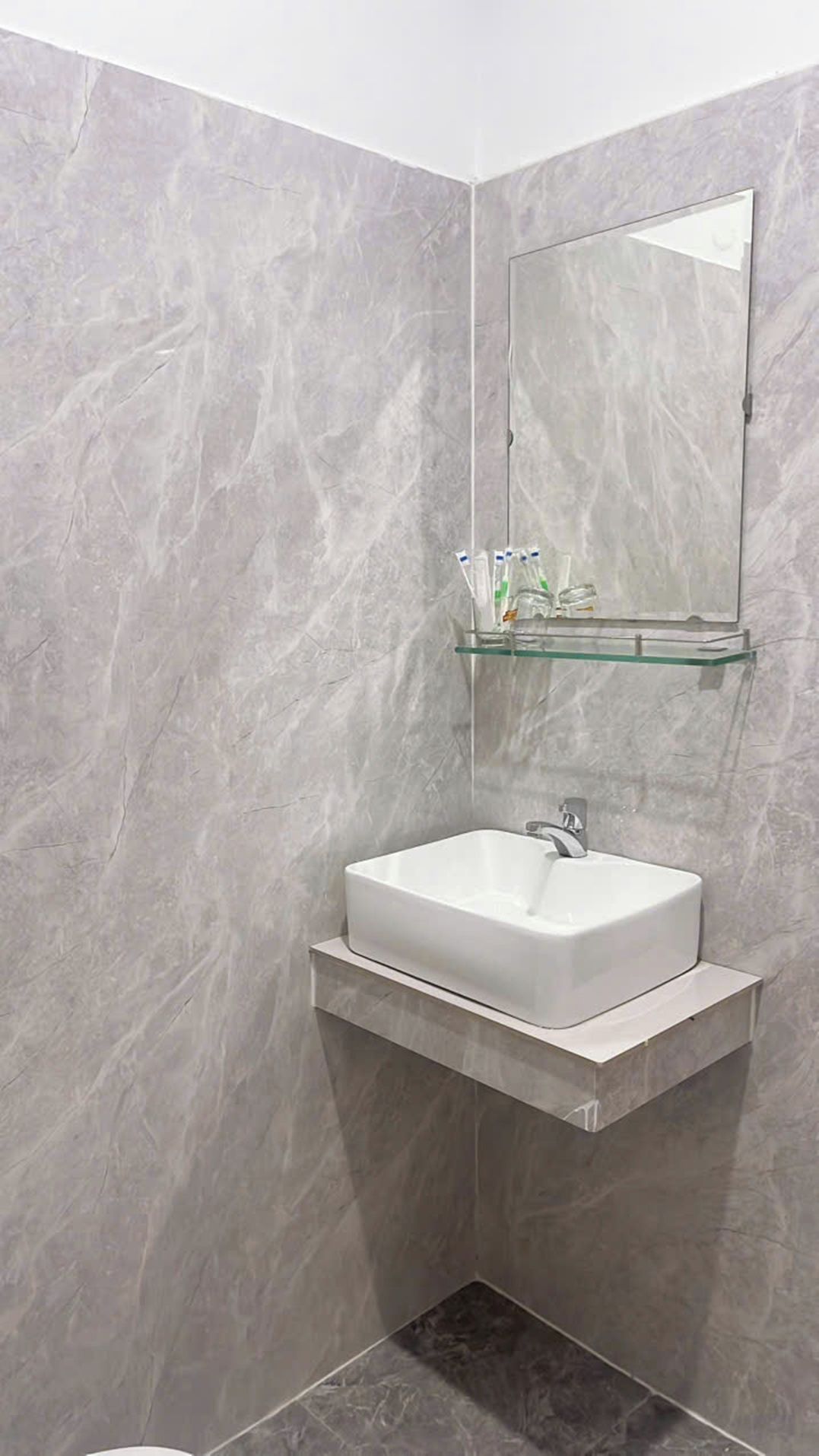A bathroom with a white sink, a mirror, and a glass shelf with toiletries.