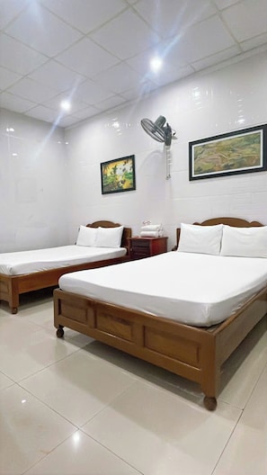 A hotel room with two wooden beds, white bedding, a wall-mounted fan, and two framed pictures. - BLUE LANTERN HOMESTAY (HOI AN)