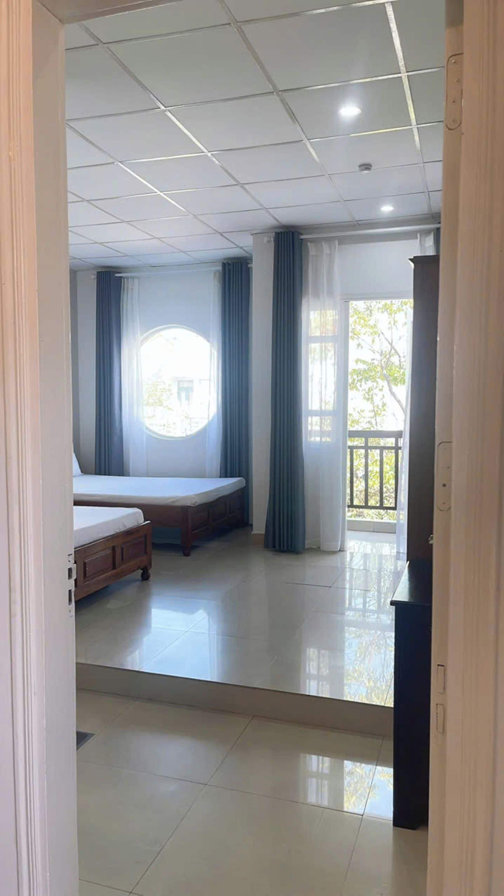 A room with a bed, a window with curtains, a balcony, and a tiled floor.