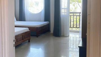 A room with a bed, a window with curtains, a balcony, and a tiled floor.