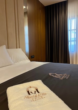 Quarto de hotel com cama, mesa de cabeceira e janela com cortinas.