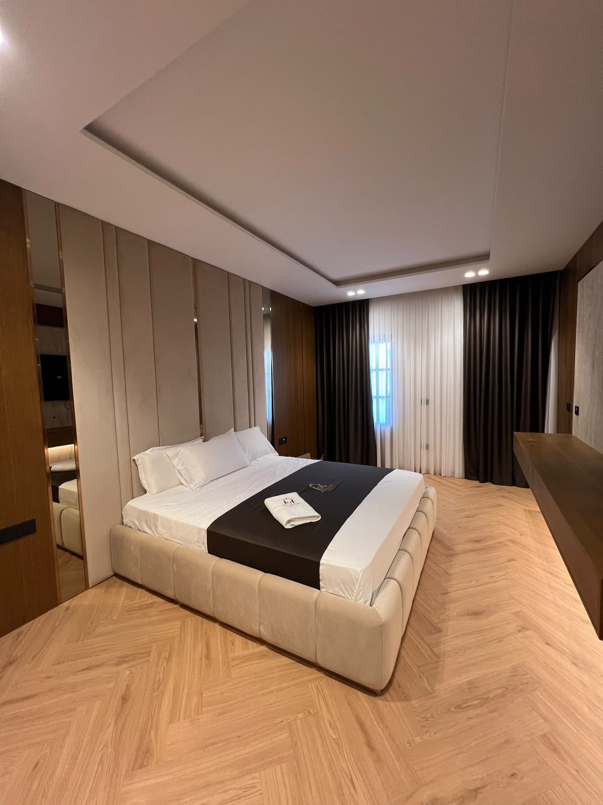 Moderni hotellihuone, jossa on suuri sänky, puulattia ja sisäänrakennettu vaatekaappi.