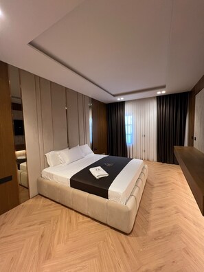 Quarto de hotel moderno com uma cama grande, piso de madeira e armário embutido.