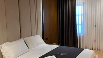 Moderni hotellihuone, jossa on suuri sänky, puinen pääty ja ikkunasta avautuva näkymä kaupunkiin.