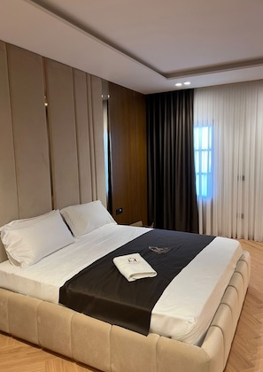 Quarto de hotel moderno com uma cama grande, cabeceira de madeira e vista para a cidade pela janela.