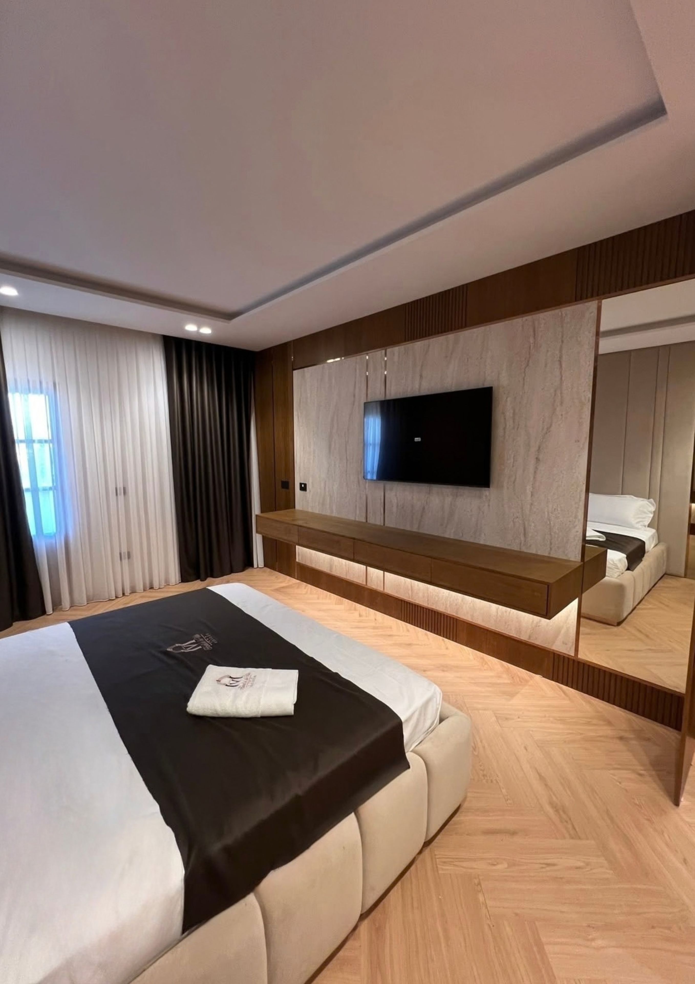 A modern bedroom with a large bed, a flat-screen TV mounted on the wall, and a wooden bench.