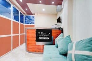 A reception area with a wooden reception desk, a sofa, and a large window. - OYO Collection O Kanpur Domestic Airport (Kanpur)