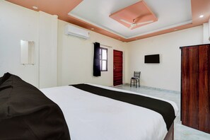 A hotel room with a bed, a chair, an air conditioning unit, and a wooden wardrobe. - OYO Collection O Kanpur Domestic Airport (Kanpur)