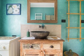 Une salle de bain avec un grand miroir, un meuble-lavabo en bois, un évier avec un bac en pierre et un porte-serviettes.