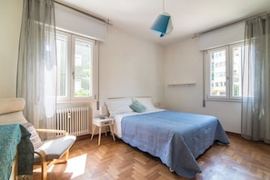 Een slaapkamer met een bed, een stoel, een nachtkastje, een lamp en een radiator.