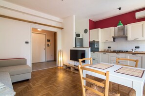 A modern kitchen with white cabinets, a microwave, and a stove. There is a dining table with chairs and a television in the living area. - New Listing (Padova)