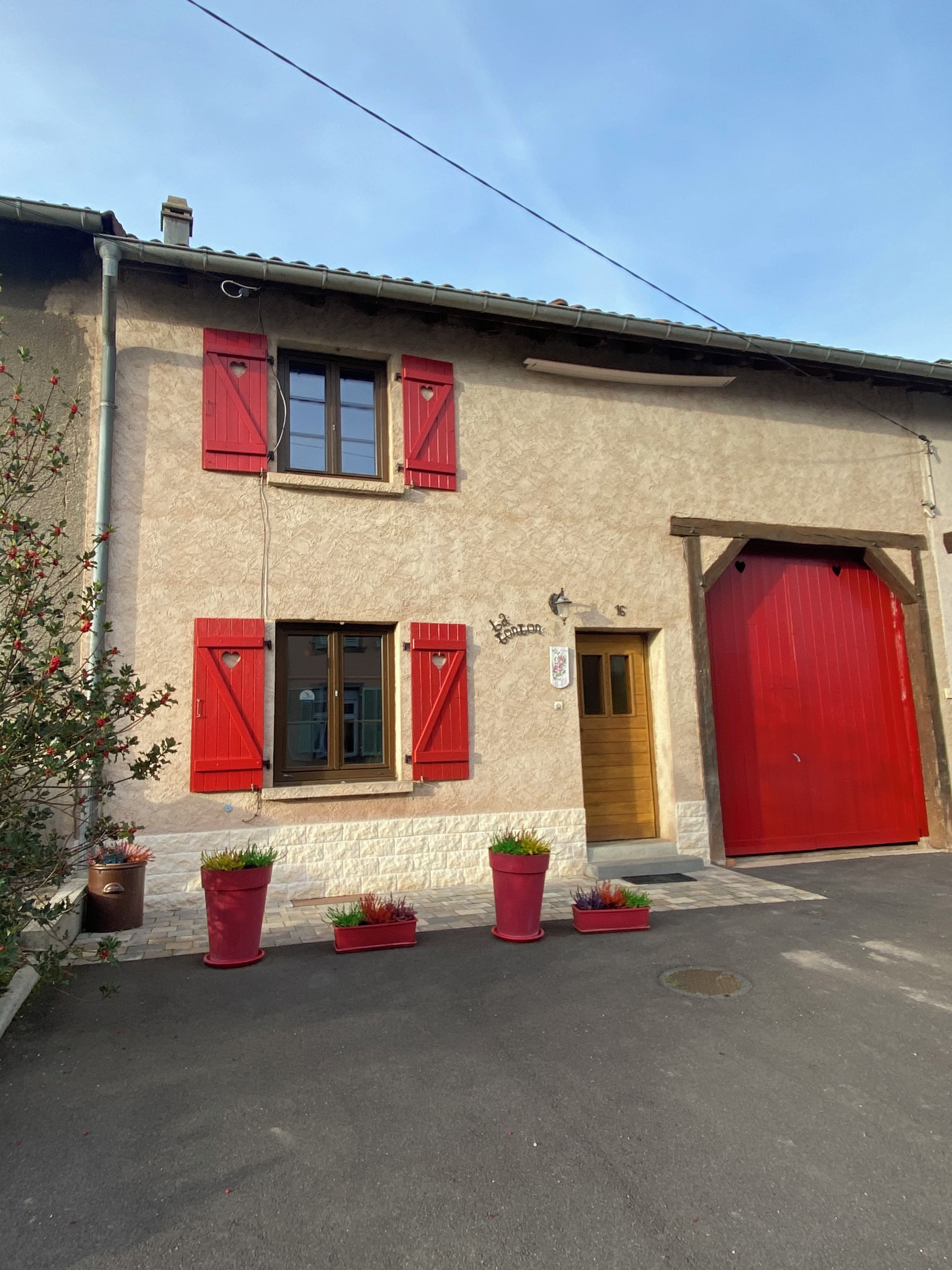 A building with a red garage door, a double door entrance, and a small window with shutters.