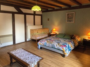 A bedroom with a wooden floor, a bed with a colorful floral bedspread, a crib, two bedside lamps, a wooden bench, and a ceiling with exposed beams. - New Listing (Desseling)