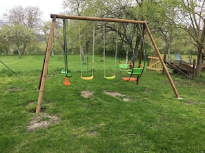 A wooden swing set with multiple swings in a grassy area. - New Listing (Desseling)