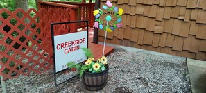 A sign for Creekside Cabin with a wooden fence and a potted plant with sunflowers. - Apartment with a Peaceful Cabin Feel and Coosawattee River Resort Amenities (Ellijay)