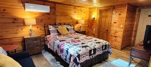 A wooden cabin bedroom with a bed, two bedside tables, a chair, and a television.