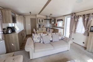 A cozy living area with a sofa, a dining table, and a kitchen in the background. - Lodge Sleeps 8 - Hot Tub - Dog Welcome (Lincoln)