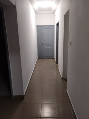 A narrow hallway with a tiled floor leading to a closed door at the end. - New Listing (Abidjan)