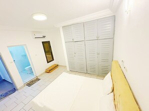 A bedroom with a bed, a wardrobe, and a bathroom visible through an open door. - New Listing (Abidjan)