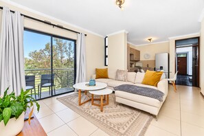 A modern living room with a sofa, a coffee table, and a view of the outdoors through large sliding doors. - Tee Off & Unwind at Jackal Creek by ctha (Roodepoort)