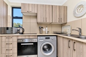 A modern kitchen with wooden cabinets, a Bosch washing machine, a microwave, and a sink. - Tee Off & Unwind at Jackal Creek by ctha (Roodepoort)