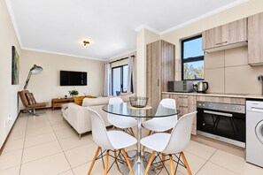 A modern apartment with a dining area, kitchen, and living space. - Tee Off & Unwind at Jackal Creek by ctha (Roodepoort)