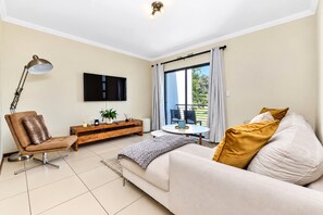 Una sala moderna con sofá, una butaca, una mesa de centro, televisor y un balcón con vistas.