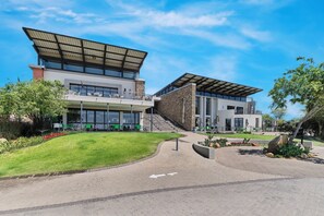 A modern building with a flat roof, large windows, and a paved entrance area. - Tee Off & Unwind at Jackal Creek by ctha (Roodepoort)