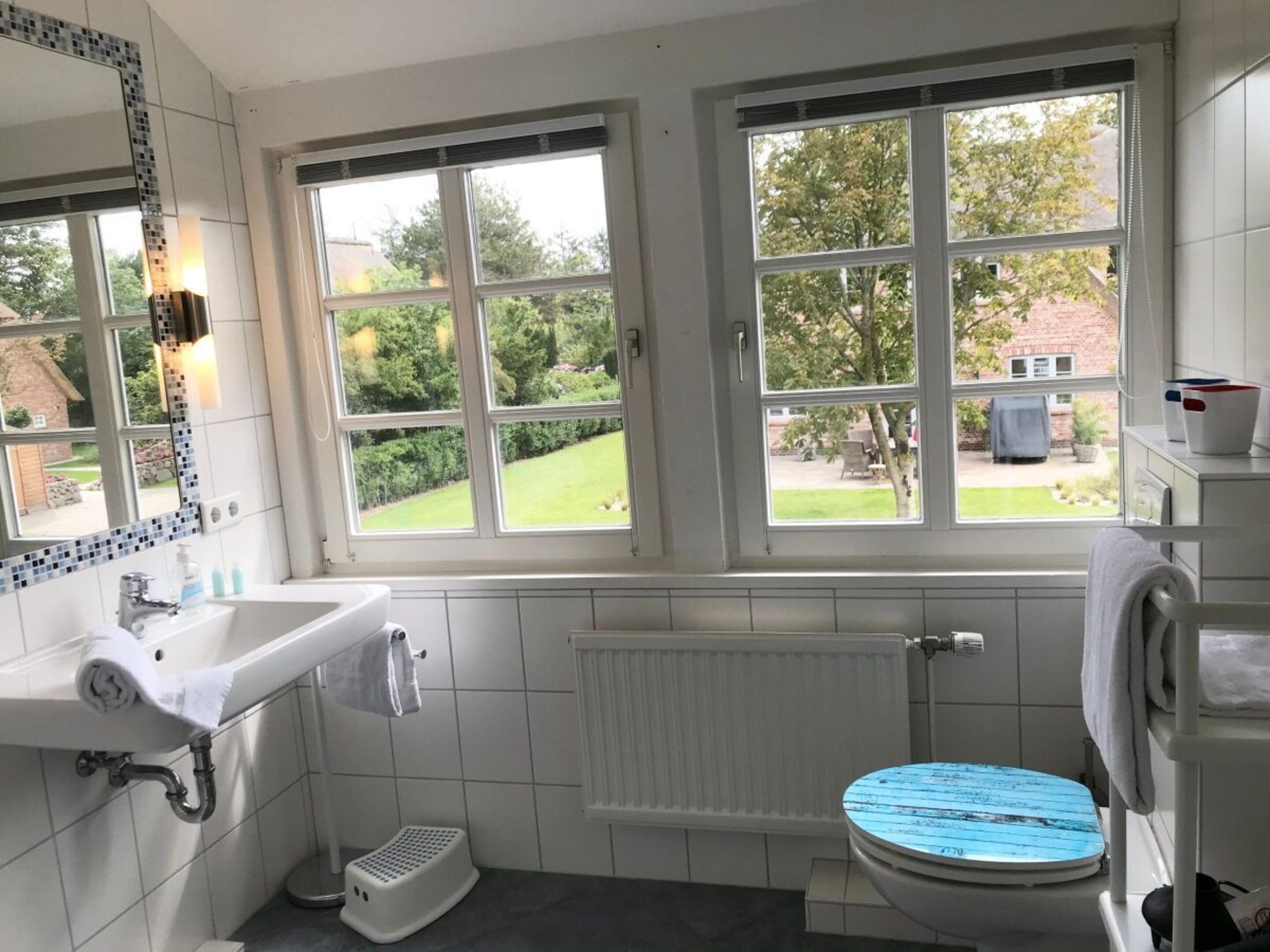 A bathroom with a white sink, a toilet, and a window with a view of a garden.