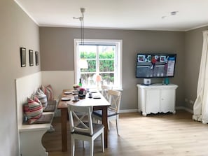 A dining area with a wooden table, white chairs, and a television on a white cabinet. - View of the Dike in Nieblum (Nieblum)