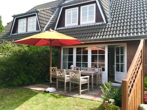 A house with a covered patio, a dining table with chairs, and a large umbrella. - View of the Dike in Nieblum (Nieblum)